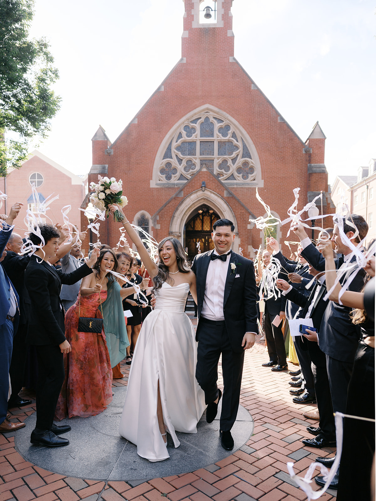 Wedding couple celebrating outside a church, surrounded by guests throwing streamer ribbons.